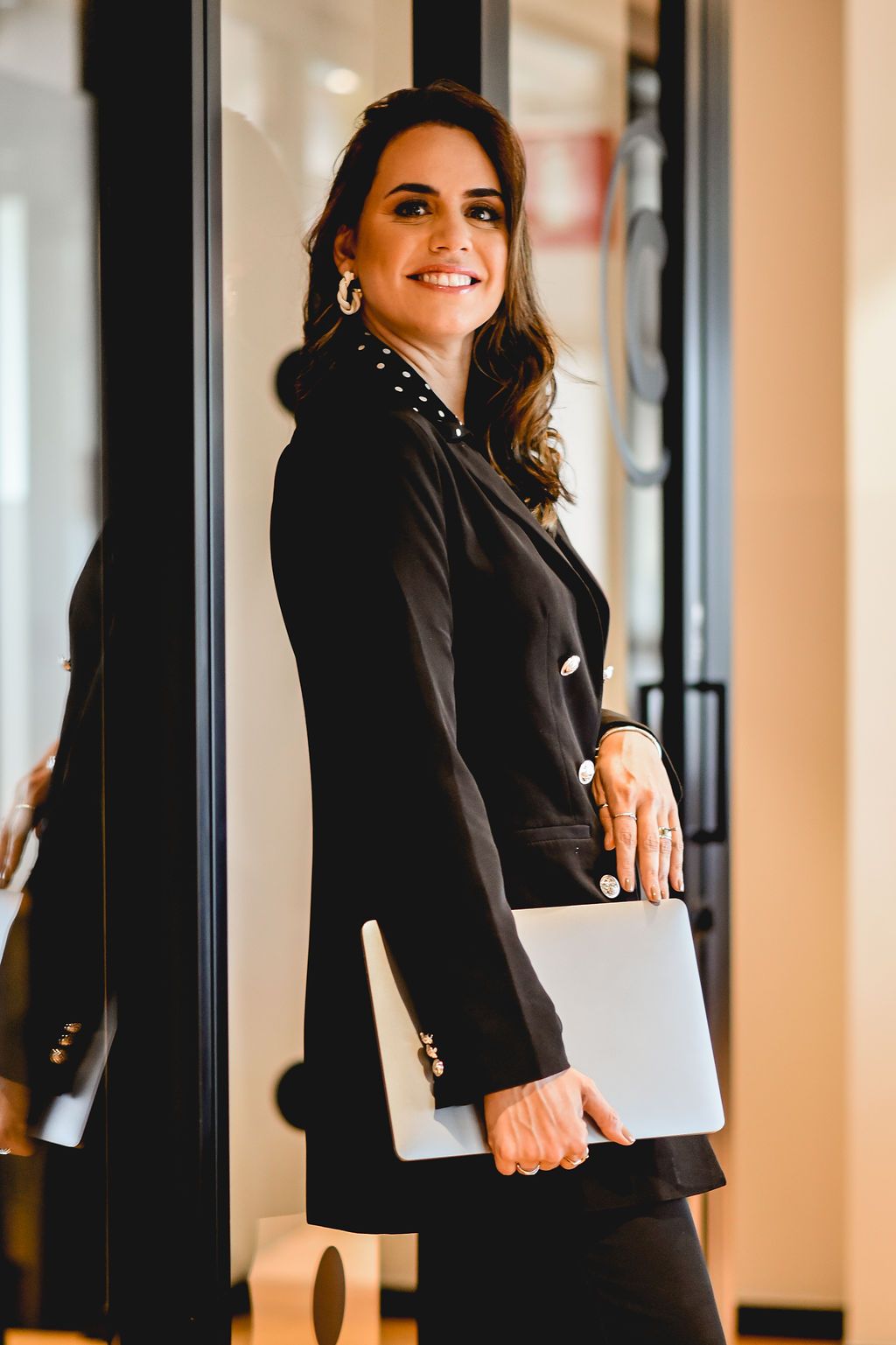 Talita Meira standing in a black blazer, holding a laptop